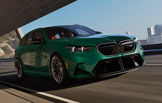 Green BMW M5 Touring driving on a city road. | BMW of Okemos in Okemos MI